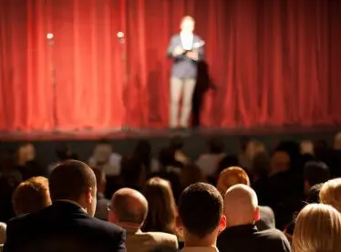Performer standing on a stage in front of an audience.