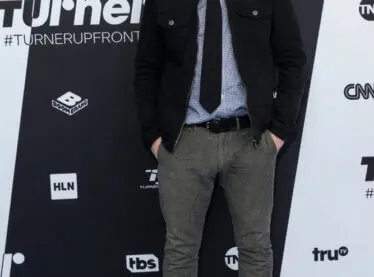 Actor and comedian Chris Gethard in a suit in front of a black and white backdrop.