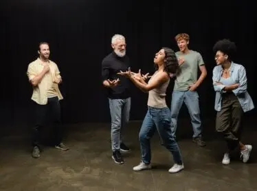 A group of acting students learning from their bearded teacher.