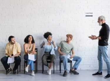A casting director in a black shirt telling a diverse group of actors which ones can go and a which ones can stay.
