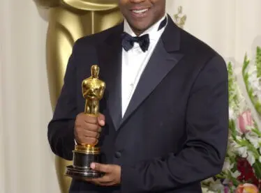 Denzel Washington in a black tuxedo holding his Oscar trophy for an incredible acting performance.