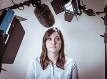 A nervous actress on an audition surrounded by lights, cameras and a mic.
