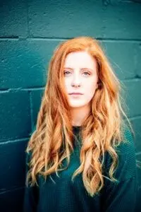 A red-headed actress in a green shirt in front of a green wall.