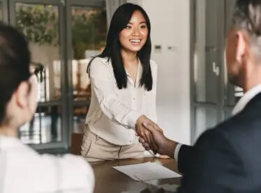 A happy Asian actress meeting with casting directors smiling and shaking hands.