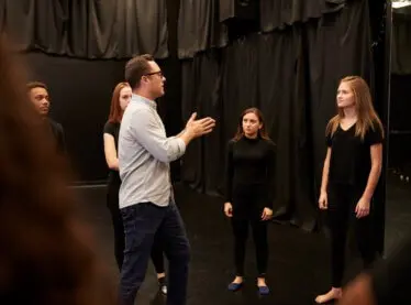 An acting teacher training his students in a room with black cutrains.