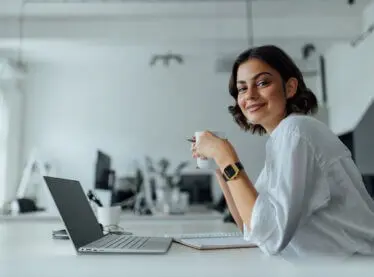 Young woman smiling and drinking tea in an office.