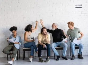 A diverse group of actors waiting to audition. Two are high-fiveing.