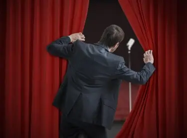 A very nervous actor experiencing stage fright peeking behind the curtain.