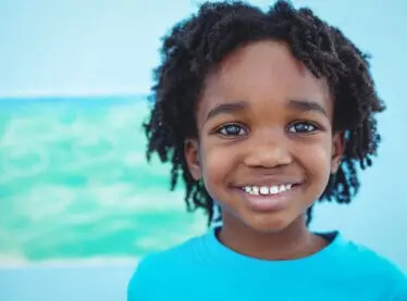 A happy African American child in front of a blue wall smiling.