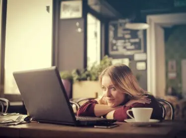 A blonde woman at a coffee shop watching an entertaining video on her laptop.