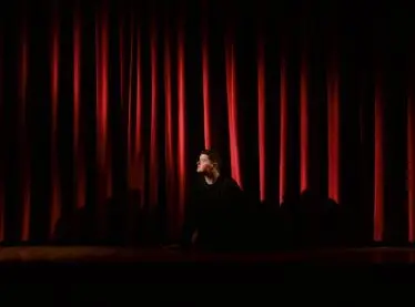 An actor sitting next to a stage, curtains are down.