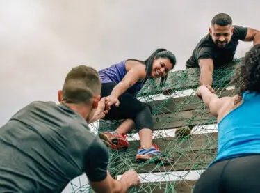 A diverse group of friends helping each other on an obstacle course.