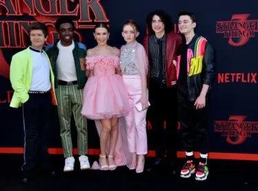 The cast of Stranger Things posing in front of a backdrop for season 3.