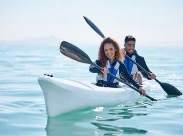 Boy and girl kayakers rowing on a lake and smiling.