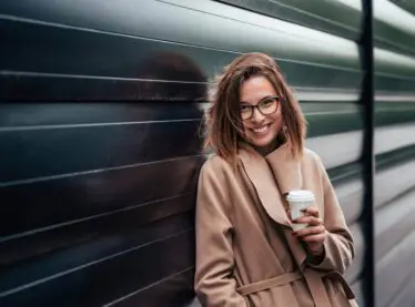 Stylish young woman with a cup of coffee by a grate.
