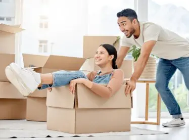Happy interracial couple moving. Asian man pushing his Spanish girlfriend in a moving box.