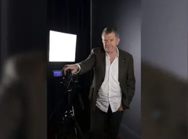 Casting director Gregory Apps smiling in a suit in front of a screen.