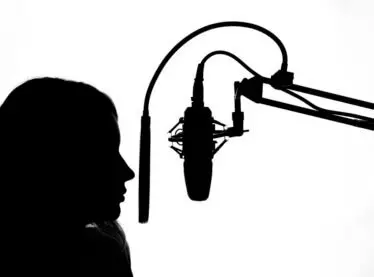 Silhouette of a femaile voice actor and a microphone on a stand in front of her as she records.