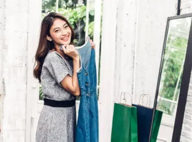 Happy asian woman admiring her new denim dress in the mirror.