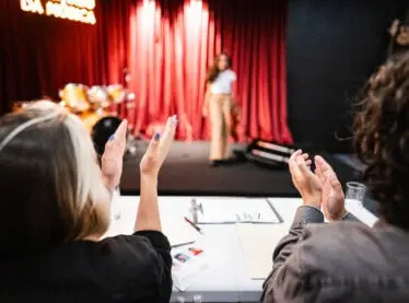 casting team applauding an acting audition. Actor is in front of a red curtain.