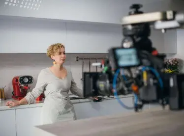 Actress in a kitchen filming a commercial, camera recording in the middle right.