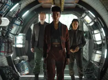 Jared Harris, Leah Harvey and Lou Llobell walking down a futuristic hallway.