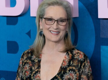 Meryl Streep smiling at an event wearing a floral shirt.