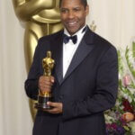 Denzel Washington in a black tuxedo holding his Oscar trophy for an incredible acting performance.