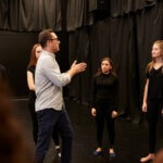 An acting teacher training his students in a room with black cutrains.