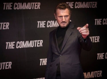 Actor Liam Neeson pointing in a suit at a premiere of the movie "The Commuter."