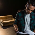Actor reading his lines on stage at rehearsal for a living room scene.