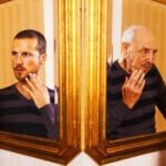 Two actors looking in the mirrors at their old and young reflections.