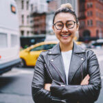 Smiling Asian woman in a leather jacket outside.