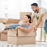 Happy interracial couple moving. Asian man pushing his Spanish girlfriend in a moving box.