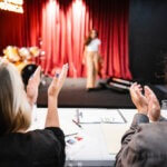 casting team applauding an acting audition. Actor is in front of a red curtain.