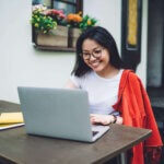 An Asian actress at home on her laptop researching self submitting for roles.