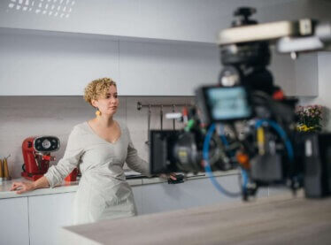 Actress in a kitchen filming a commercial, camera recording in the middle right.