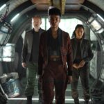 Jared Harris, Leah Harvey and Lou Llobell walking down a futuristic hallway.