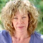 Casting director Kathryn Brink smiling outside in a blue shirt with poofy blonde hair.