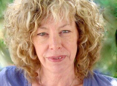 Casting director Kathryn Brink smiling outside in a blue shirt with poofy blonde hair.